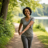 A smiling person in their late 40s enjoying a casual walk on a path next to a lake, conveying a sense of active well-being and ease of movement.