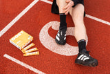 An athlete sitting on a red running track massaging their calf, alongside a box and individual sachets of OOST liquid marine collagen for active recovery.
