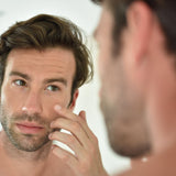 Image of man in mirror inspecting skin care